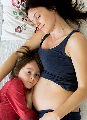 This is an image of a pregnant woman cuddling with her young son in bed. Click here to learn more about how Araya can help with Family Health.