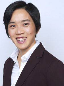 Photo of Dr. Khanita, smiling in a burgundy jacket and white button shirt, against a solid light grey background.